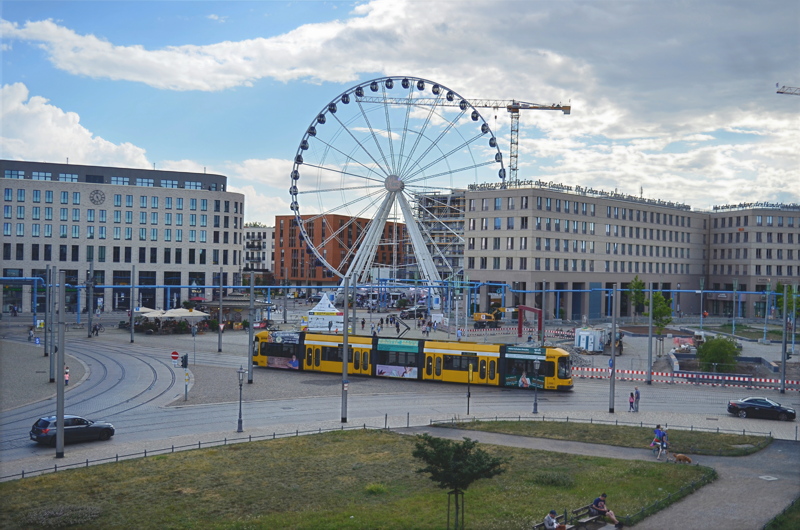 13 - The bustling Postplatz square in Dresden, Germany, featuring the temporary 55-meter-tall Wheel of Vision Ferris wheel and a yellow DVB tram passing through the major public transit hub